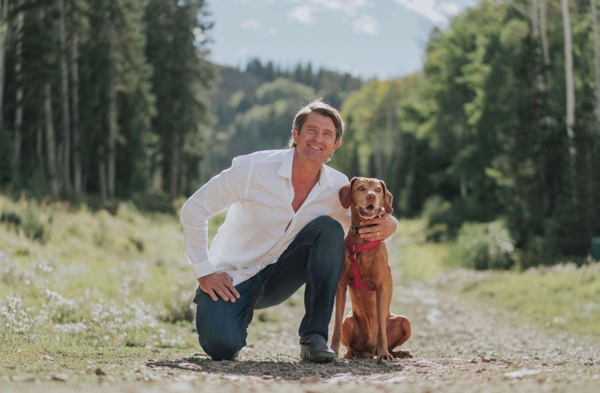 Michael kneeling outdoors beside his red dog